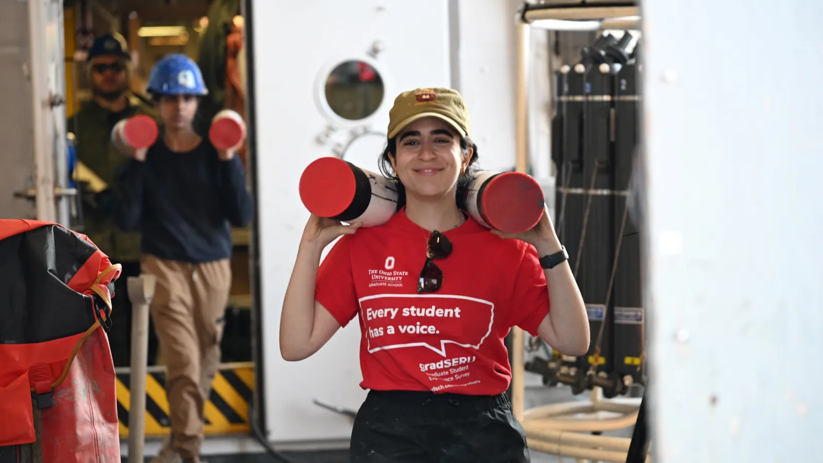 Batoul walking while carrying two sections of a jumbo piston core.