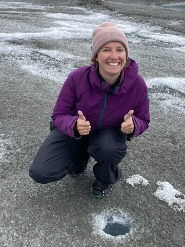 Girl on Greenland Ice Sheet giving thumps up next to borehole.