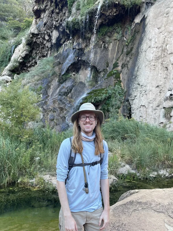 Graduate student Max Eshbaugh standing outside in front of a small waterfall